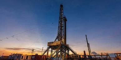 Oil drilling rig silhouetted against a sunset sky.