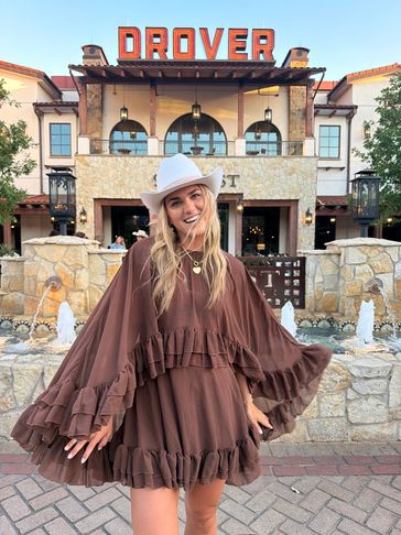 Woman in a brown dress and white hat smiling outside Drover building.