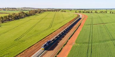 A freight train travels through vast green fields on a sunny day.