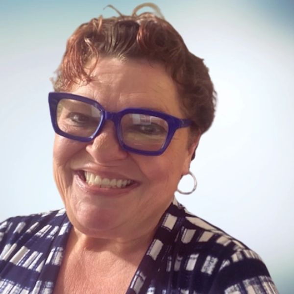 Smiling woman with short curly hair and blue glasses.
