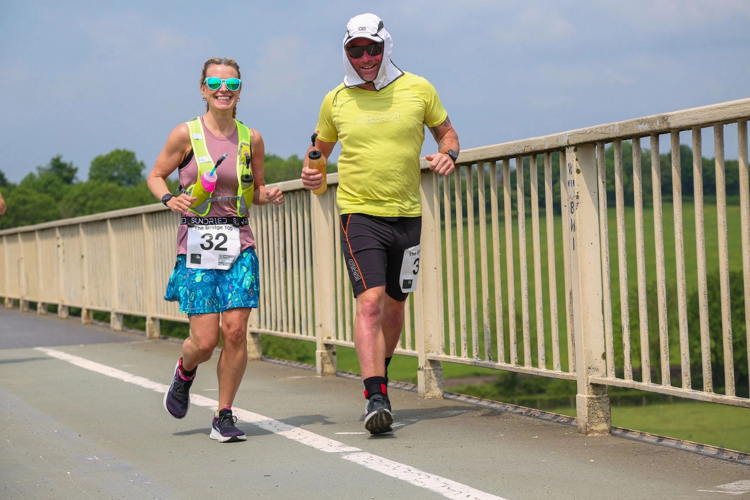 Two happy runners participating in a ultra marathon race on a bridge.