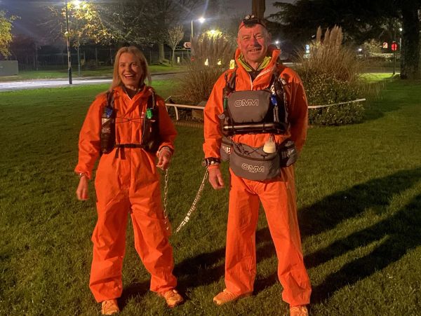 Two people in orange suits at night, linked by a chain.