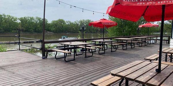 Empty outdoor patio with picnic tables and red umbrellas by the river.