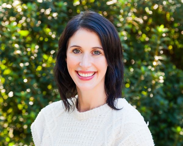 Smiling woman with dark hair wearing a white sweater outdoors.