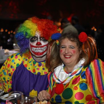 Two people in clown costumes with colorful wigs and face paint.