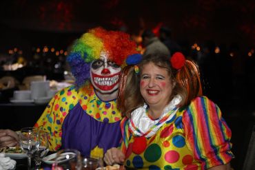 Two people dressed as colorful clowns with big smiles at a party.