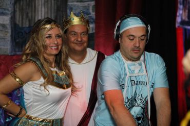 Three people in costumes, one woman, one man in a crown, and a DJ.