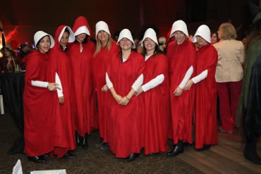 Group dressed as Handmaids from The Handmaid's Tale in red cloaks and white bonnets.