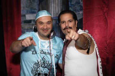 Two men pointing at the camera, one wearing headphones.