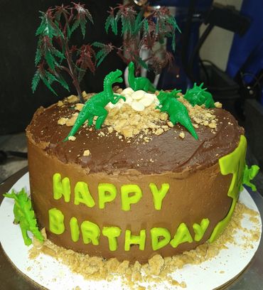 Custom round 8inch chocolate dinosaur cake with happy birthday on the front and toy dinosaurs on top