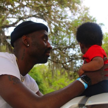 Man holding a child outdoors with trees in the background.