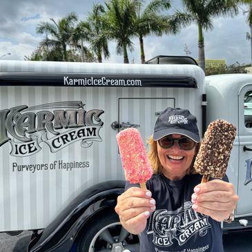 Debbie of Karmic Ice Cream holding up two Ice Cream pops  in front of 1935 Karmic Ice Cream truck