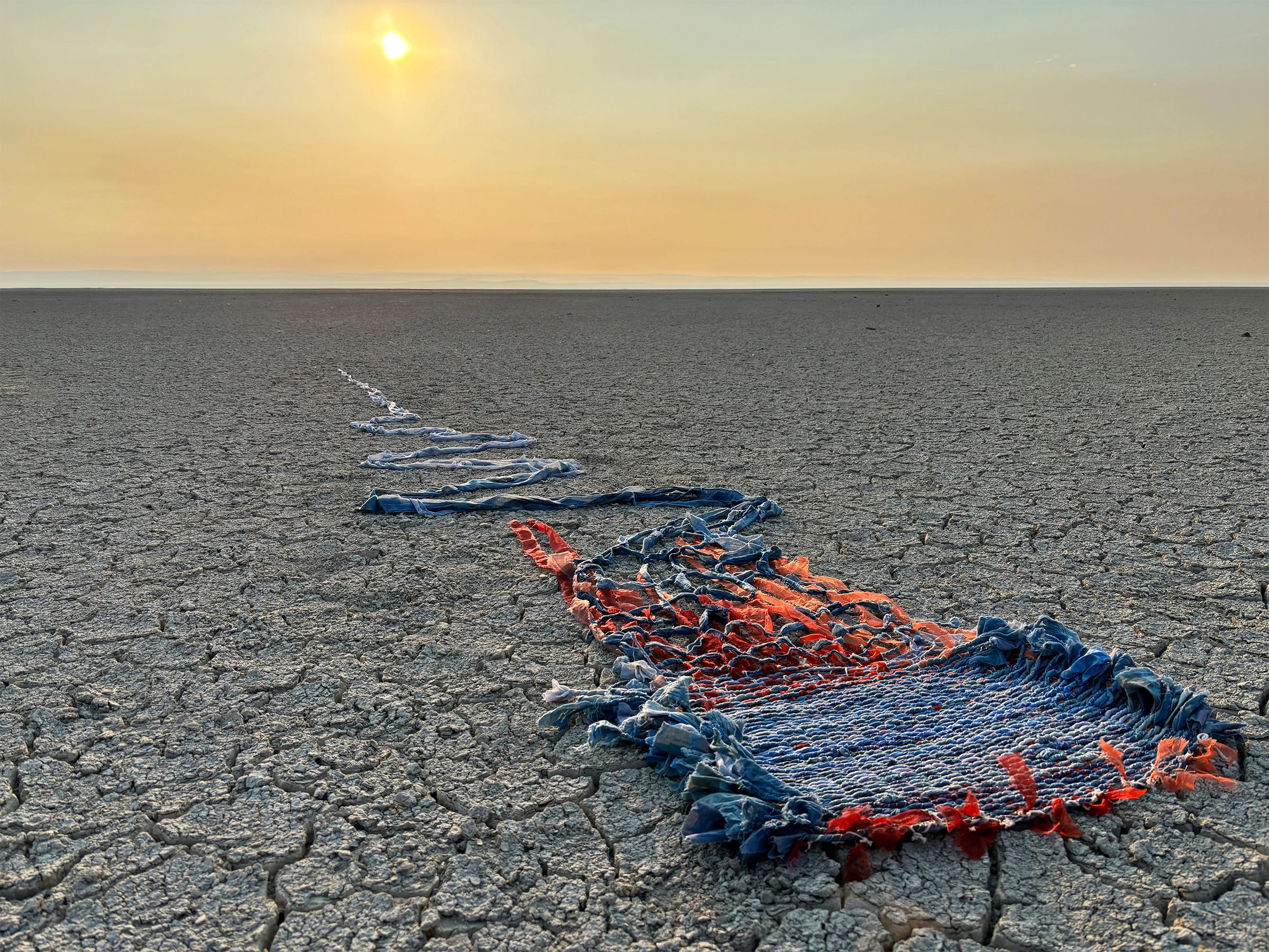 Worn-out rug on cracked desert ground at sunset.