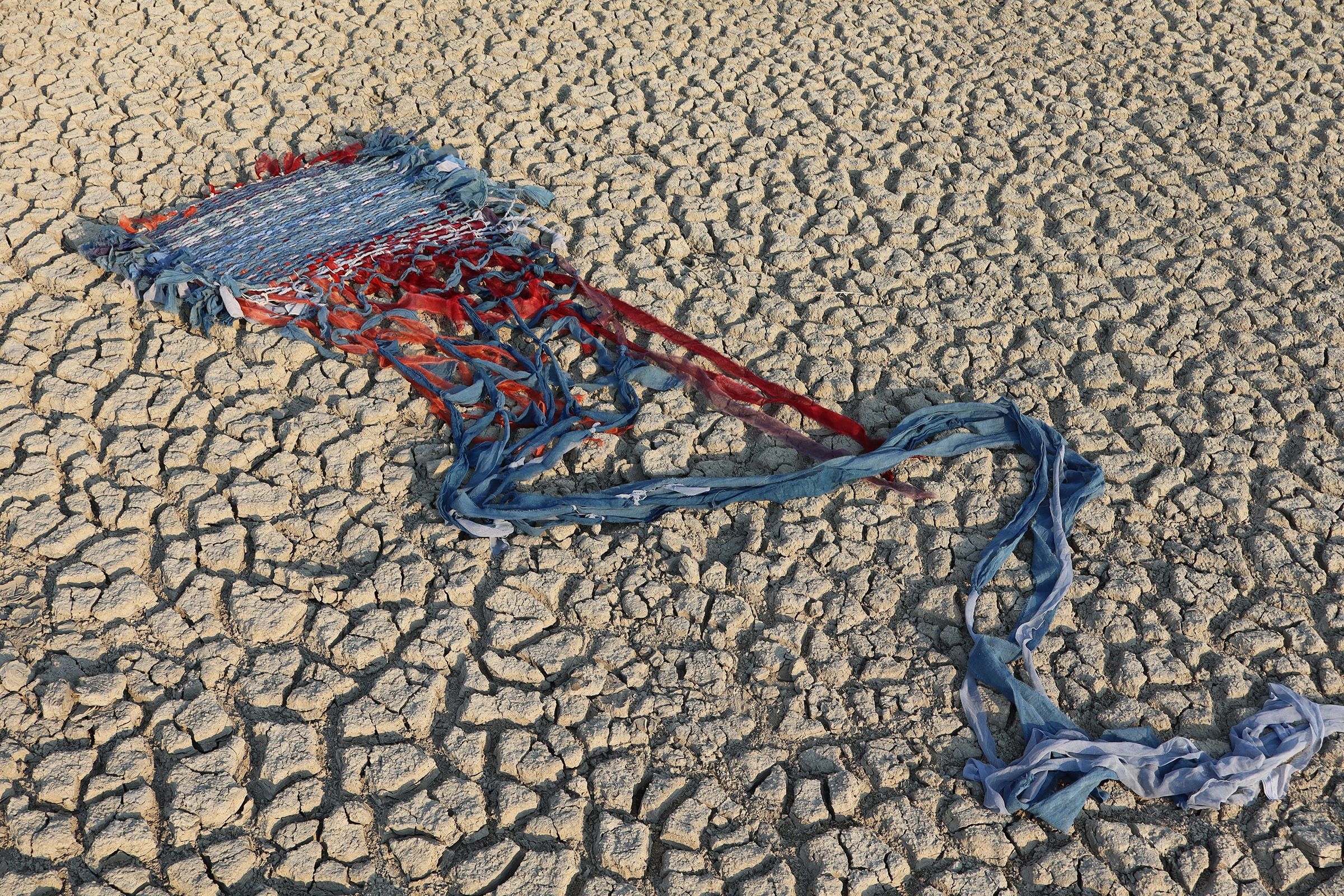 Colorful woven fabric on dry cracked ground.