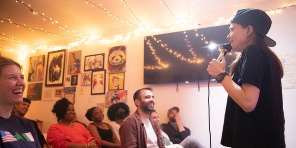 Comedian performing to a lively audience in an intimate room.
