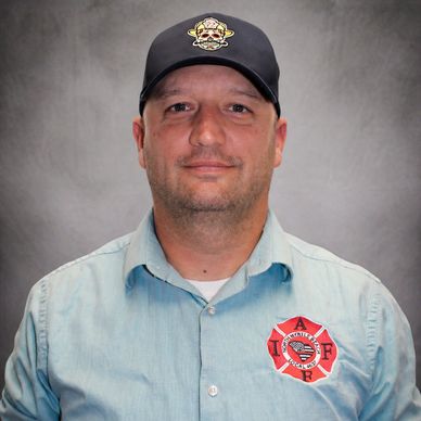 Man in firefighter uniform shirt and cap with emblem.