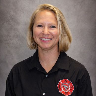 Smiling woman in a black firefighter shirt with emblem.