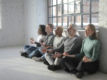 Five diverse adults meditating together in a bright, minimalist room.