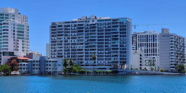 Modern buildings by a calm blue waterfront under a clear sky.