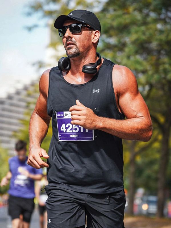 A muscular man running in a marathon wearing black sportswear and sunglasses.