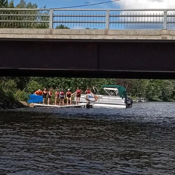 People in life jackets preparing on a dock under a bridge near a boat.