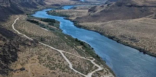 A winding river flowing through a dry, hilly landscape with dirt roads.