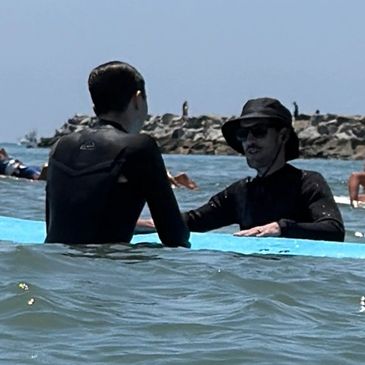 two gentleman standing in the ocean with a surfboard