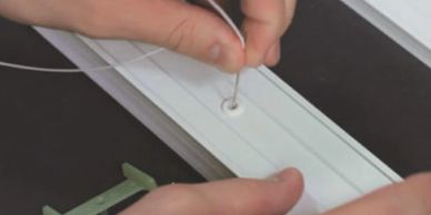 Hands threading a thin wire through a small hole in a white plastic strip.