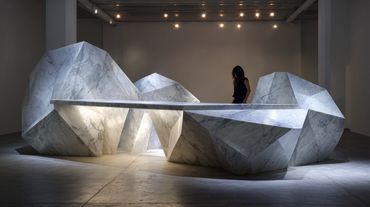 Geometric stone bench art installation with a person sitting in the background.