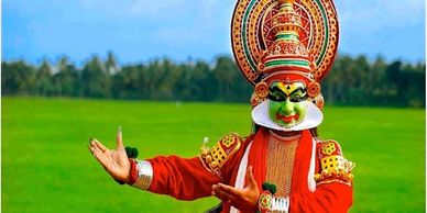 A performer in vibrant traditional Kathakali costume dances outdoors.