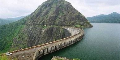 A curved dam with a mountain in the background and water on one side.