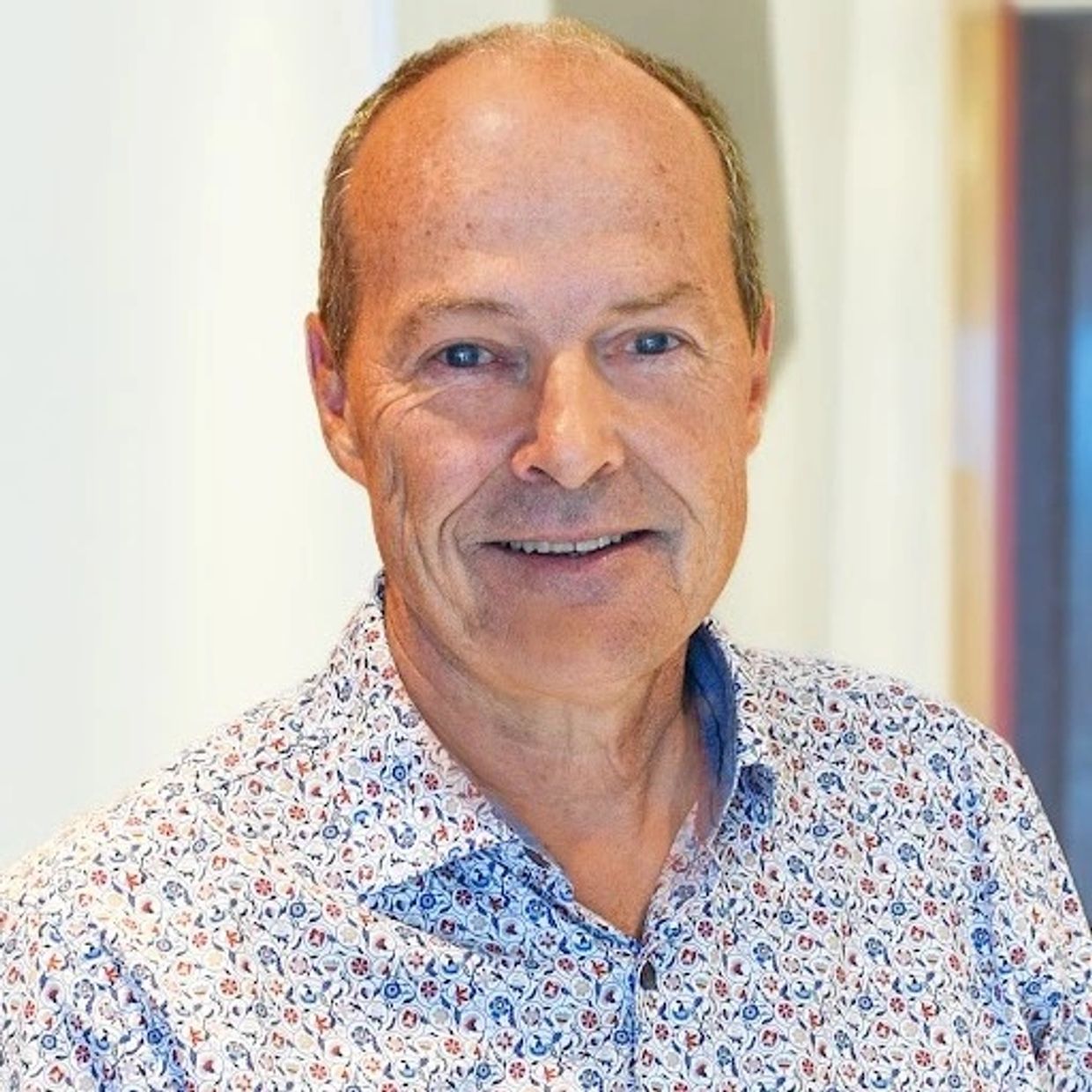 Portrait d'un homme souriant en chemise à motifs.