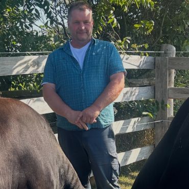 Man standing outdoors near wooden fence and animals.