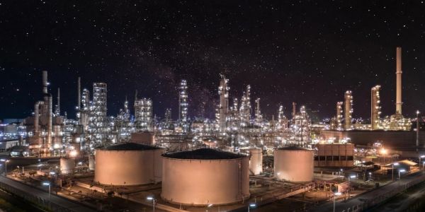 Illuminated oil refinery tanks and towers under a starry night sky.
