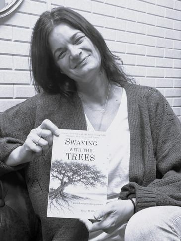 Woman smiling, holding a book titled 'Swaying with the Trees'.