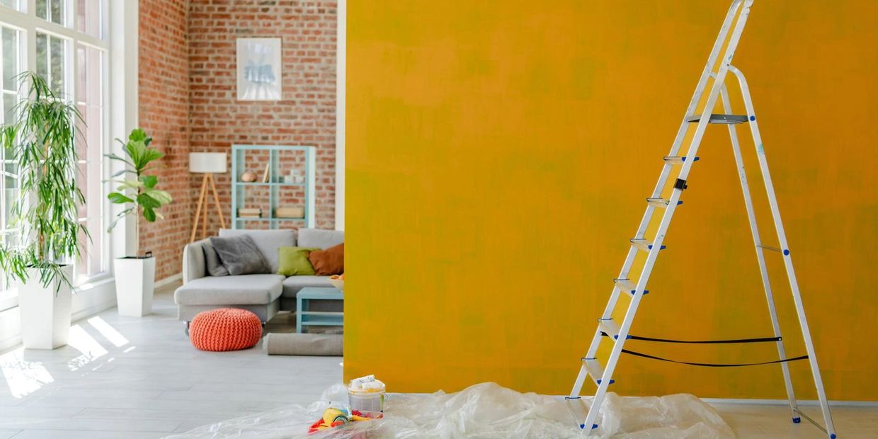 A bright yellow painted wall with a ladder and a cozy living room in the background.
