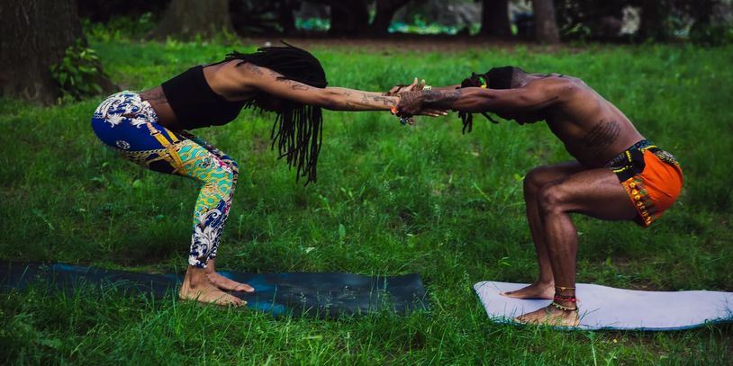 Two people practicing partner yoga outdoors on mats in a green park.