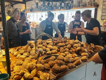A bakery display filled with various breads and pastries with bakers in the background.