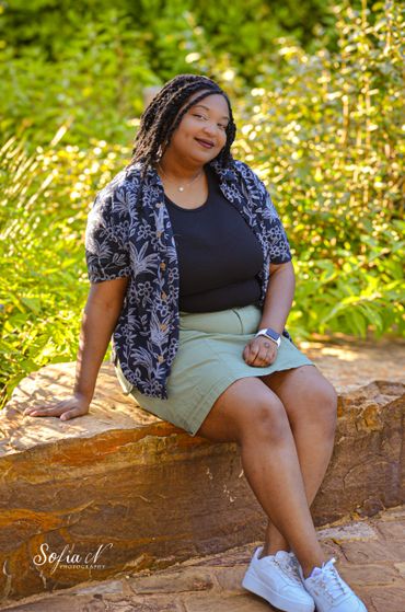 Woman smiling while sitting on a stone ledge in a sunny garden.
