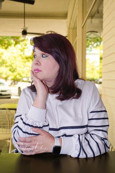 Woman with purple hair gazing thoughtfully while resting her chin on her hand.