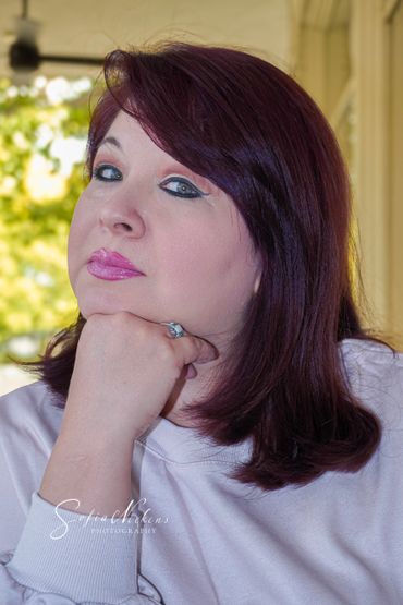 Woman with auburn hair and pink lipstick posing thoughtfully with hand under chin.