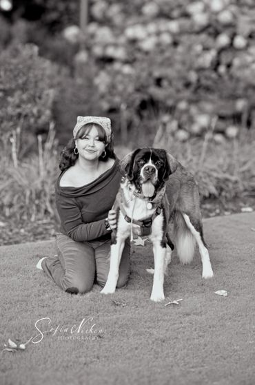 Woman kneeling on grass with a large dog, both looking at the camera.