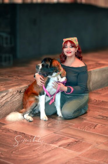 A woman kneeling and hugging a large dog indoors on tiled floor.