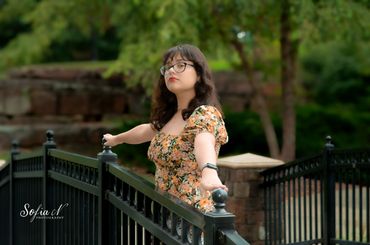 Woman in floral dress posing confidently on a black metal fence outdoors.