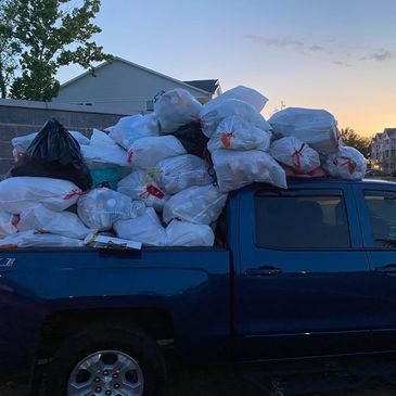 Pickup truck overloaded with numerous trash bags at dusk.