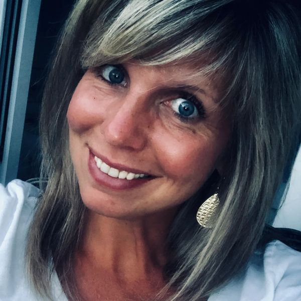 Smiling woman with blue eyes and highlighted hair wearing gold earrings.