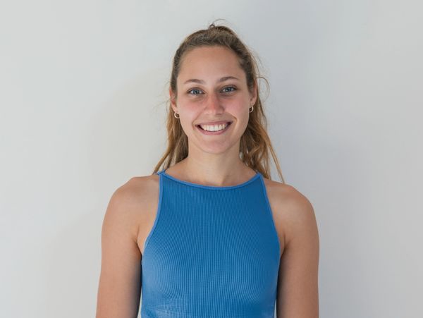 Smiling young woman in a blue sleeveless top against a plain background.