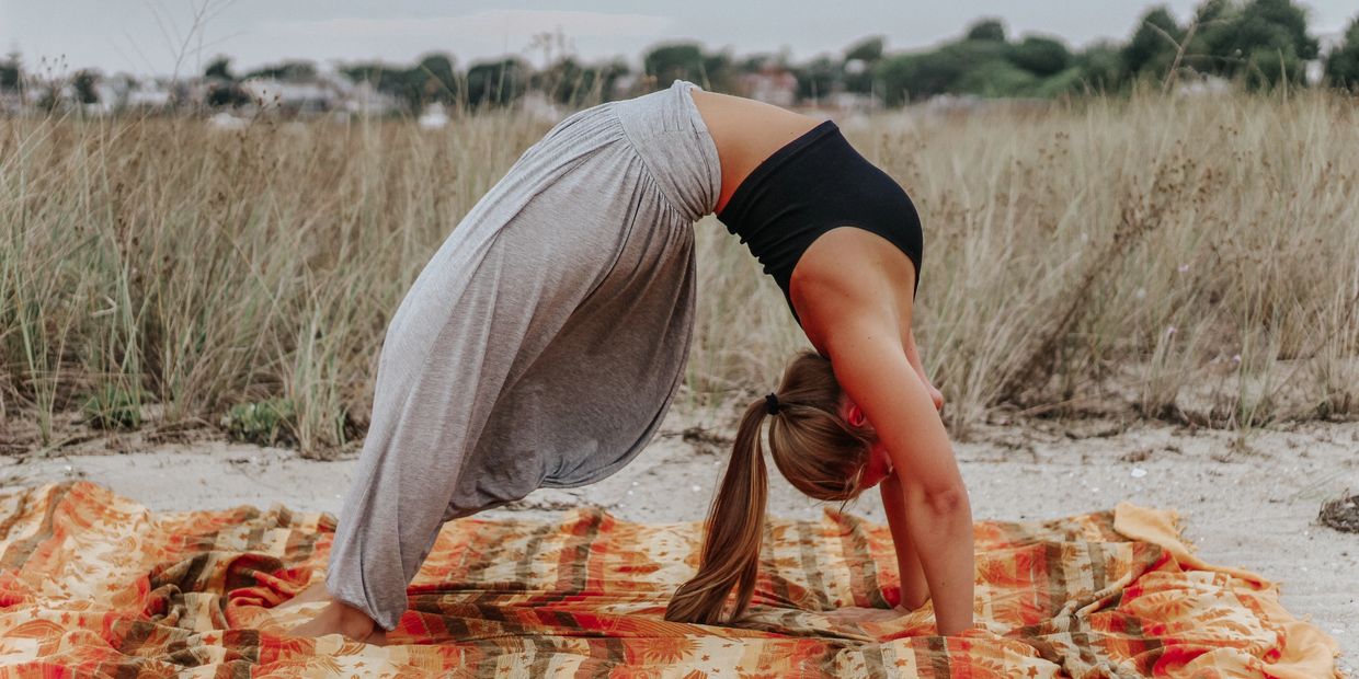 Woman practicing yoga in a backbend pose on a patterned blanket outdoors.