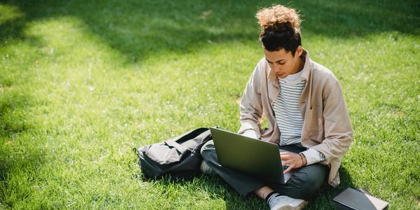Young man sitting on the grass working on a laptop