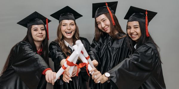 Four girls holding diplomas wearing their graduation caps & gowns.